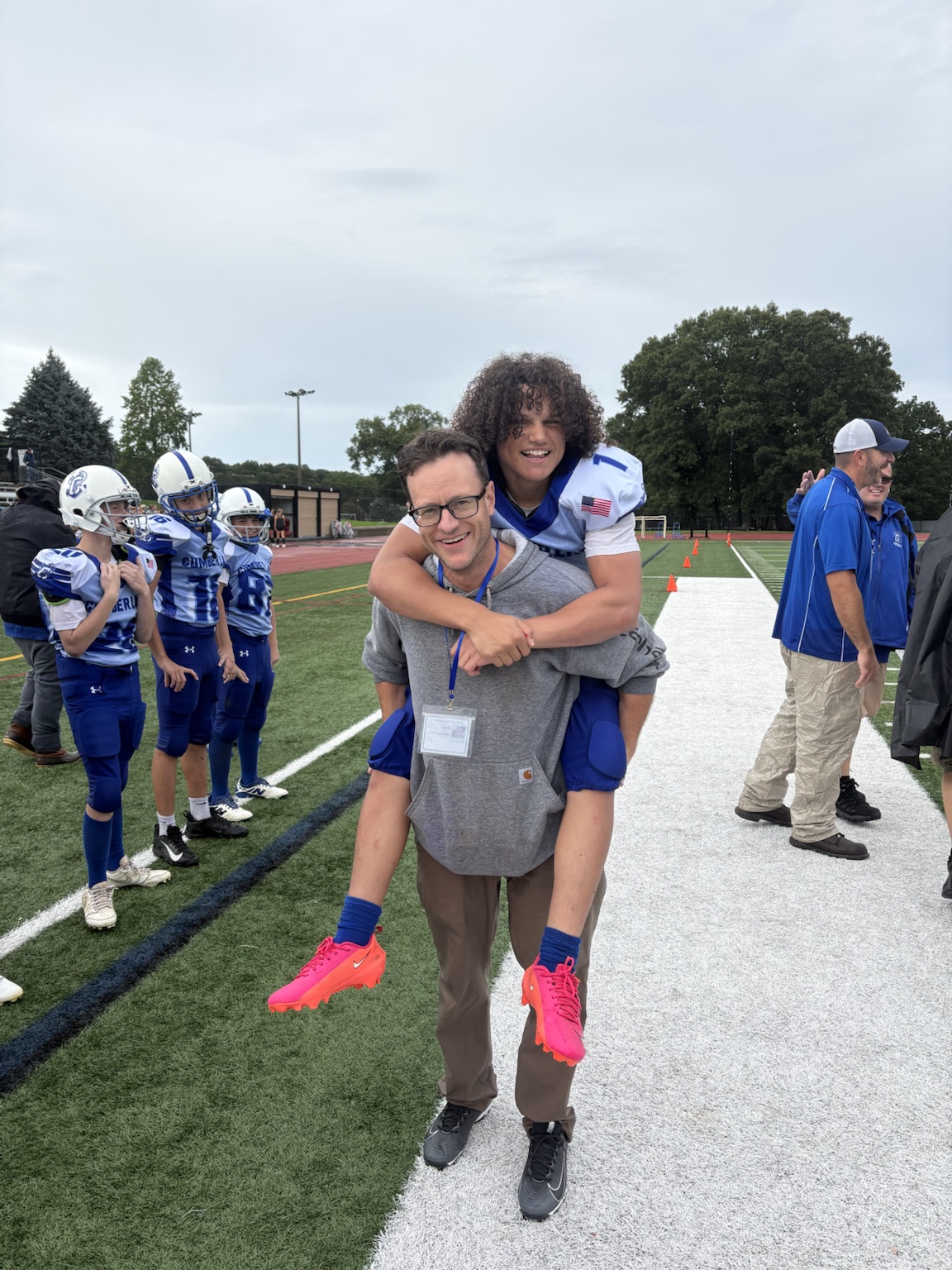 A Cumberland football player on an adult’s back, smiling on the sideline